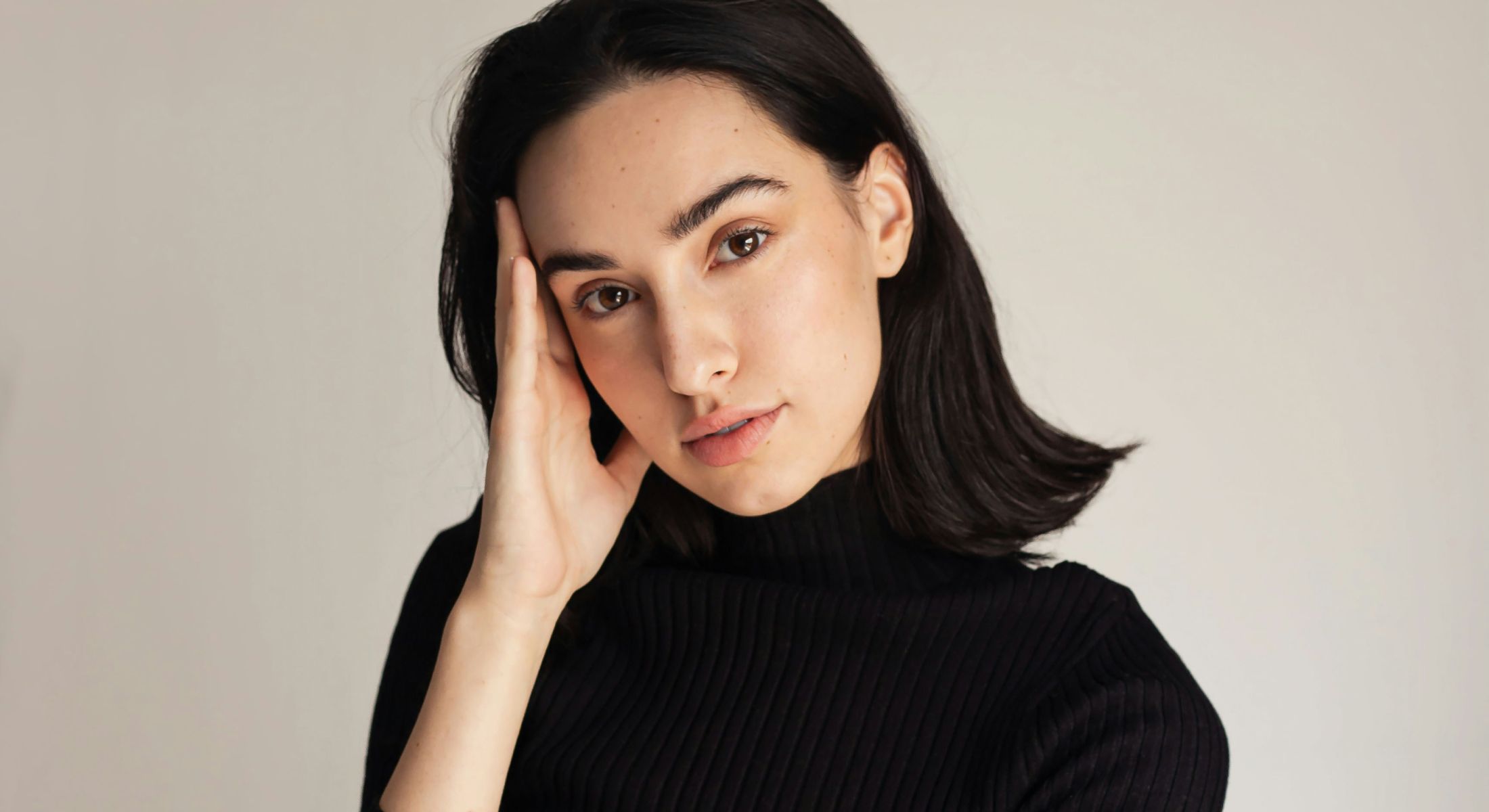 Young woman with dark hair in thoughtful pose.